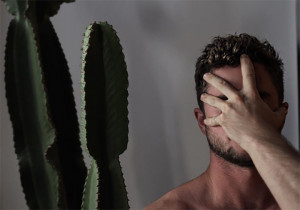 man with hand over face next to a cactus