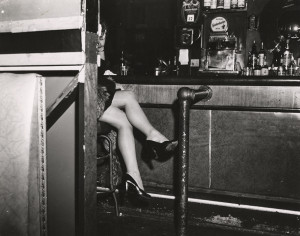 A woman is partially visible as she sits on a bar stool at a bar, her legs are crossed; in the background are bottles of liquor, New York, ca.1940s. (Photo by Weegee (Arthur Fellig)/International Center of Photography/Getty Images)