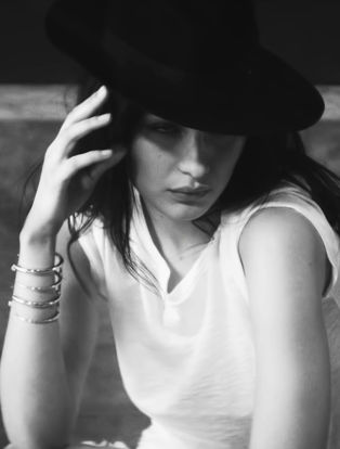 bella hadid posing with hand on face and wearing a black hat