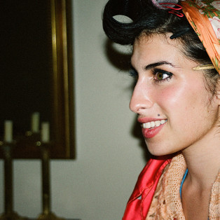 woman holding a photograph of amy winehouse in a head wrap and biting her lip