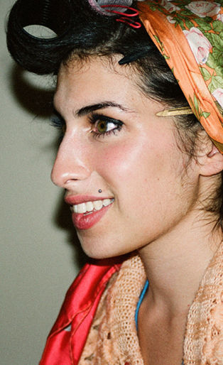 woman holding a photograph of amy winehouse in a head wrap and biting her lip