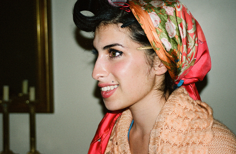 woman holding a photograph of amy winehouse in a head wrap and biting her lip