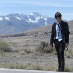 Nick Robinson wearing a suit, tie and backpack on roadside, being charlie movie