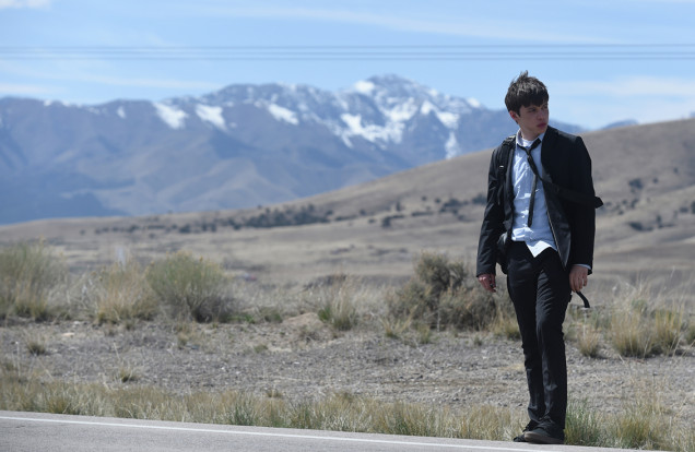 Nick Robinson wearing a suit, tie and backpack on roadside, being charlie movie