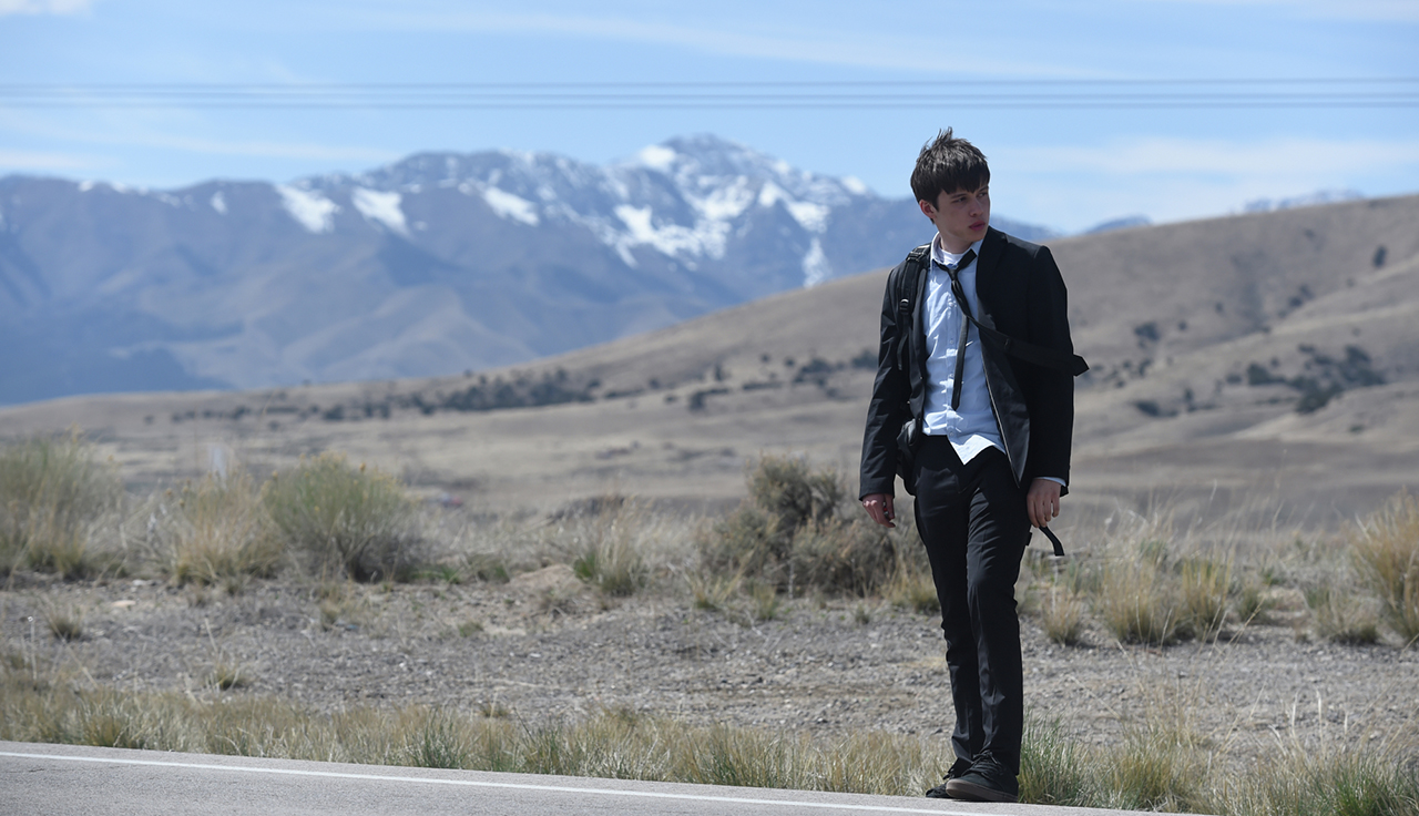 Nick Robinson wearing a suit, tie and backpack on roadside, being charlie movie