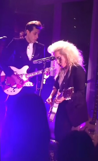 lady gaga and mark ronson playing guitar together on stage in purple light