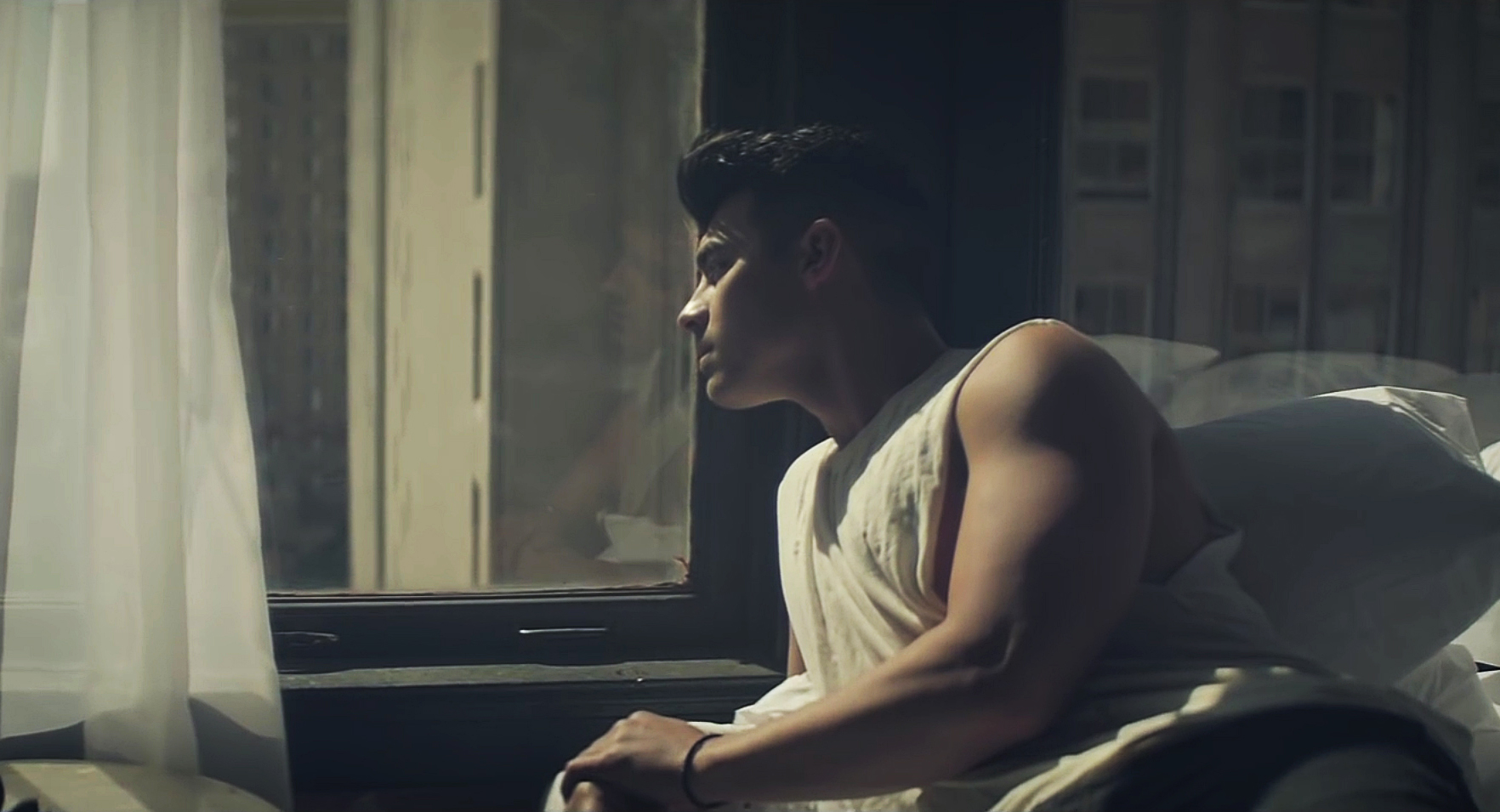 joe jonas staring out a window while wearing a sleeveless t shirt