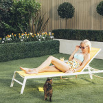 girl sun bathing on a chair with a cat surrounded by greenery