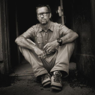 Eric Clapton. Timothy White, 1997. Sitting in a doorway, arms on knees.
