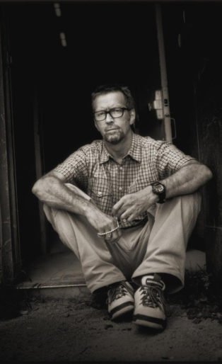 Eric Clapton. Timothy White, 1997. Sitting in a doorway, arms on knees.