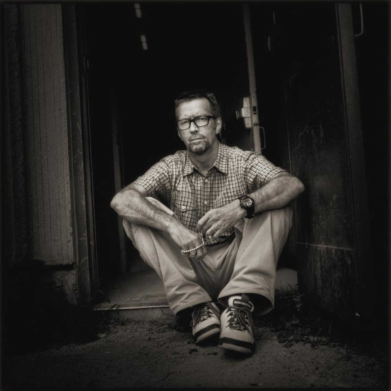 Eric Clapton. Timothy White, 1997. Sitting in a doorway, arms on knees.