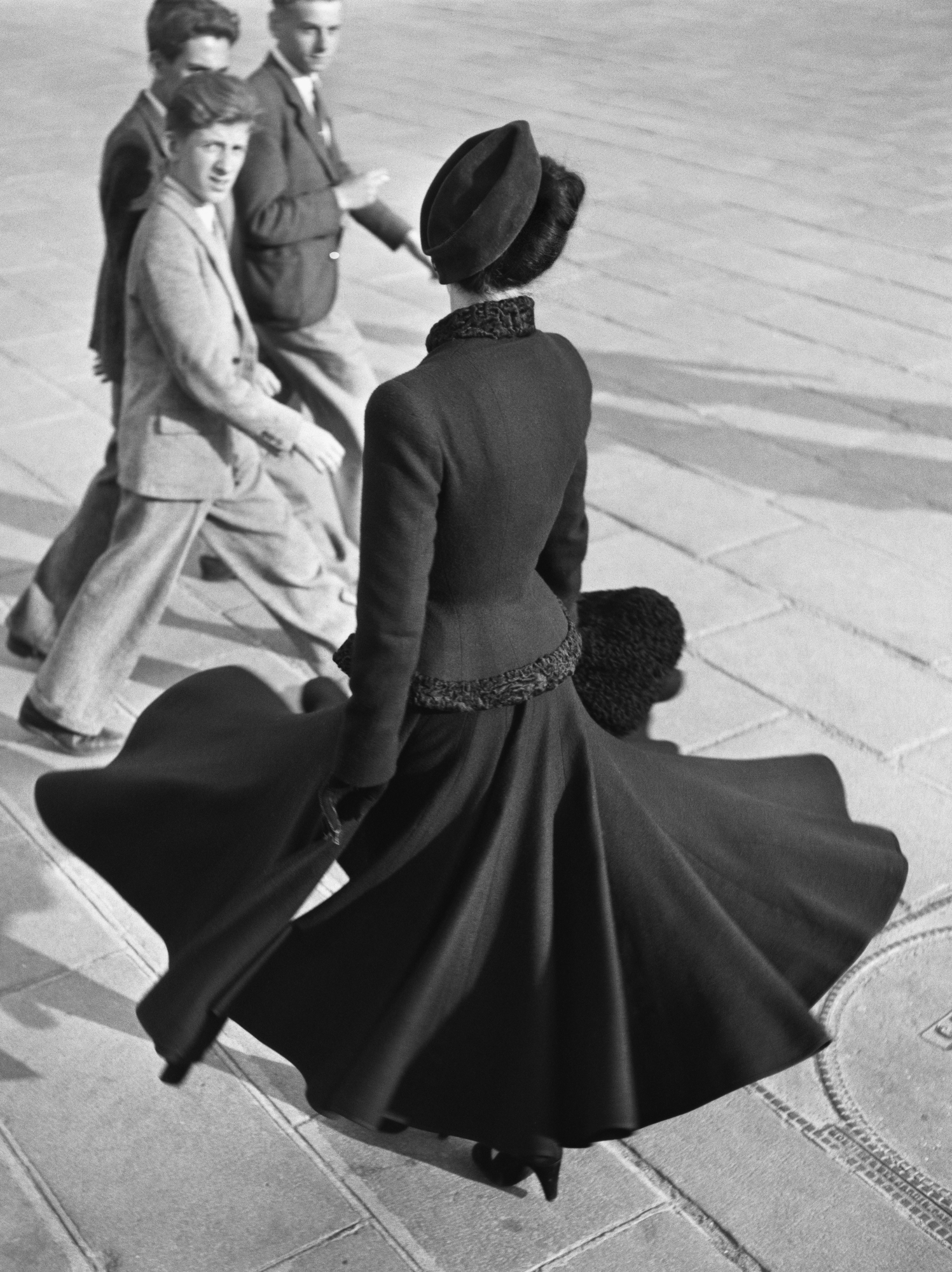 Woman in black fashion on street with three men in suits watching