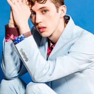 Troy Sivan white suit sitting elbows on knees
