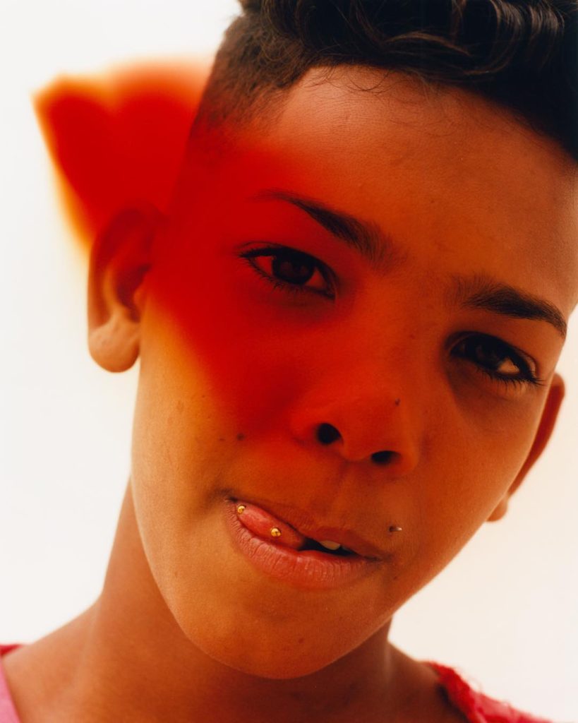 Tyler Mitchell Photograph of a Young Androgynous Face Shrouded in Red with Pierced Tongue