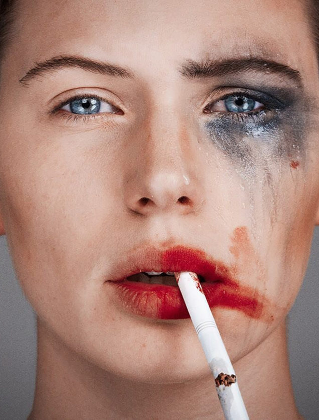 Tyler Shields photograph of a women with one side of her face with smeared make up and a cigarette dangling from her right side of her lip and the left side of her face all clean