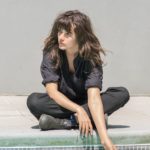Courtney Barnett sitting by pool hand in water