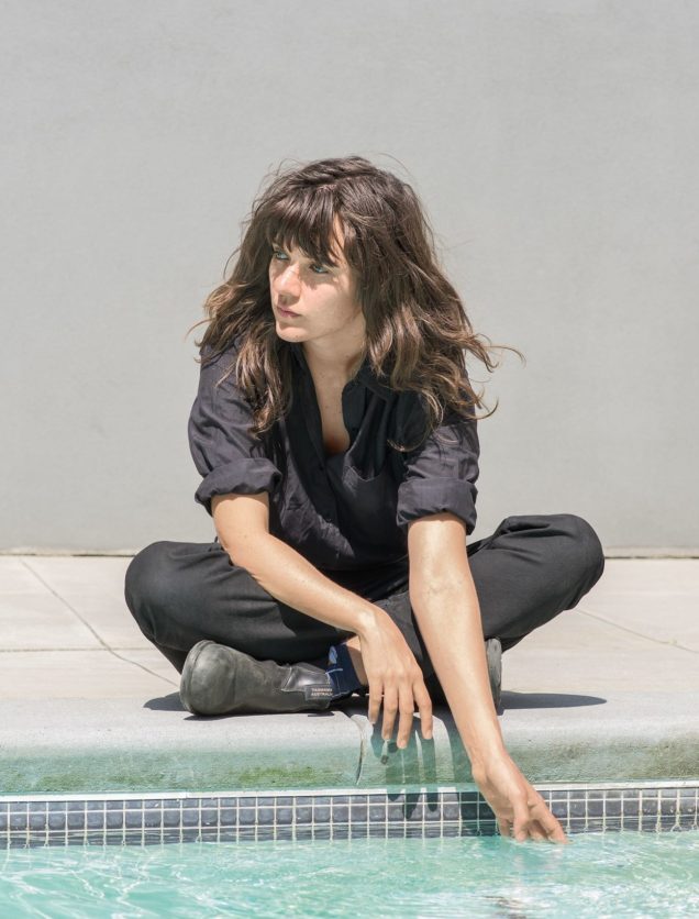 Courtney Barnett sitting by pool hand in water