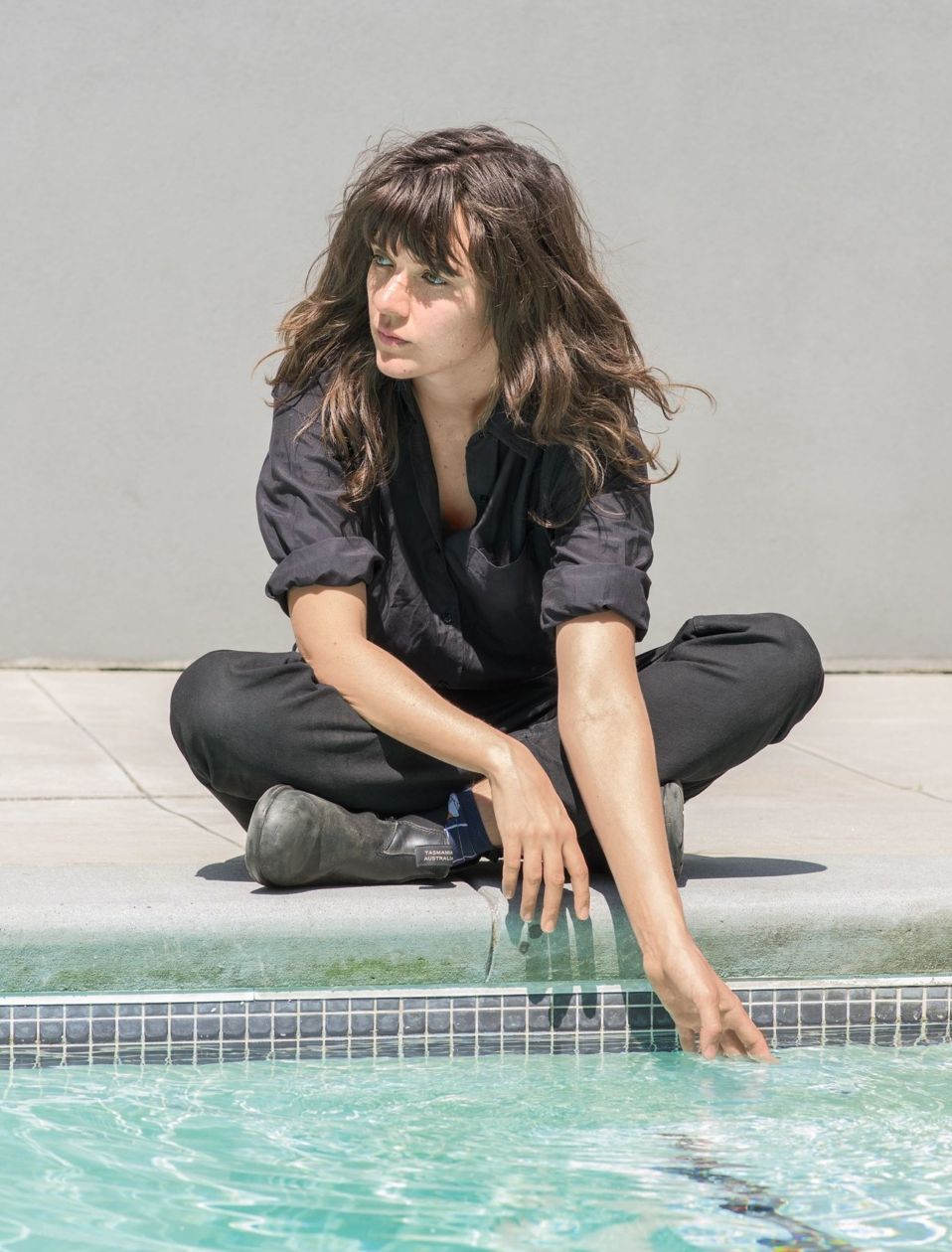 Courtney Barnett sitting by pool hand in water