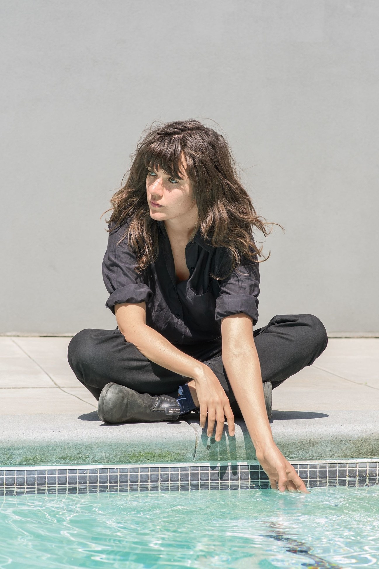 Courtney Barnett sitting by pool hand in water