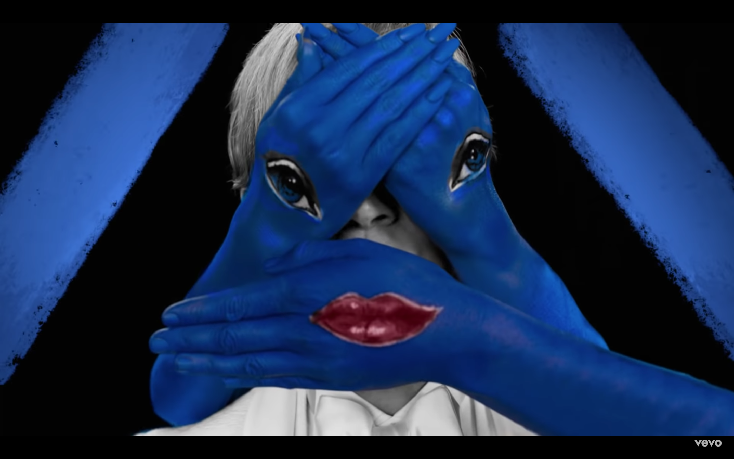 Screen shot of Beck's face hidden by three blue hands: one with lips and the other two with eyes from Beck's New Music Video, Colors, October 2018