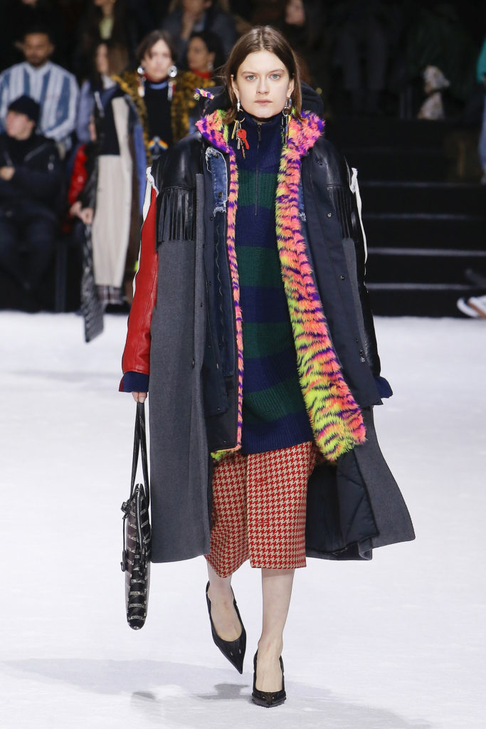 Female Runway Model Wearing Gray Coat with Black Leather Trim on the shoulders, blue and green zipper sweater, pink, purple and yellow fur jacket and red checked skirt-Balenciaga Collection