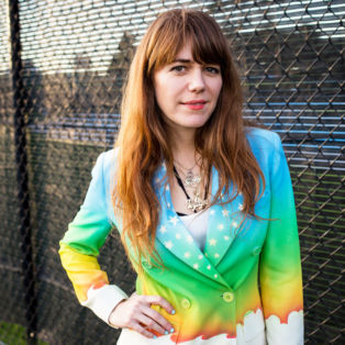 Jenny Lewis rainbow jacket in front of fence