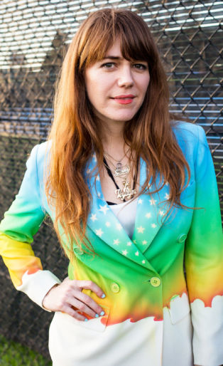 Jenny Lewis rainbow jacket in front of fence