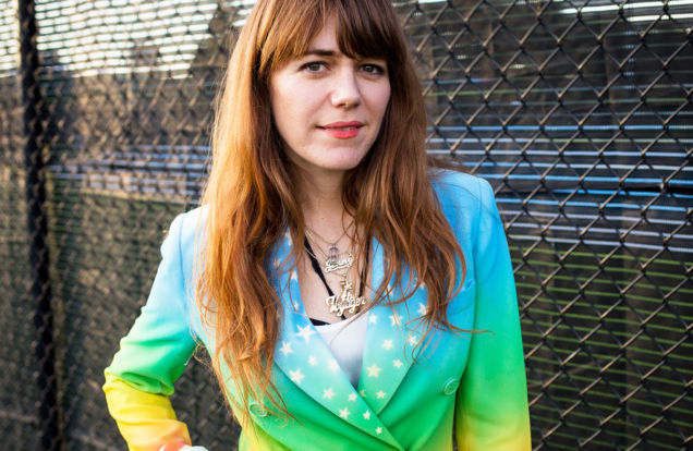 Jenny Lewis rainbow jacket in front of fence