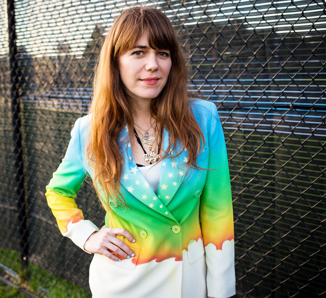 Jenny Lewis rainbow jacket in front of fence