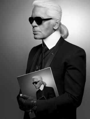 Karl Lagerfeld Holding a Magazine that shows Karl Largerfeld wearing the same outfit he is wearing