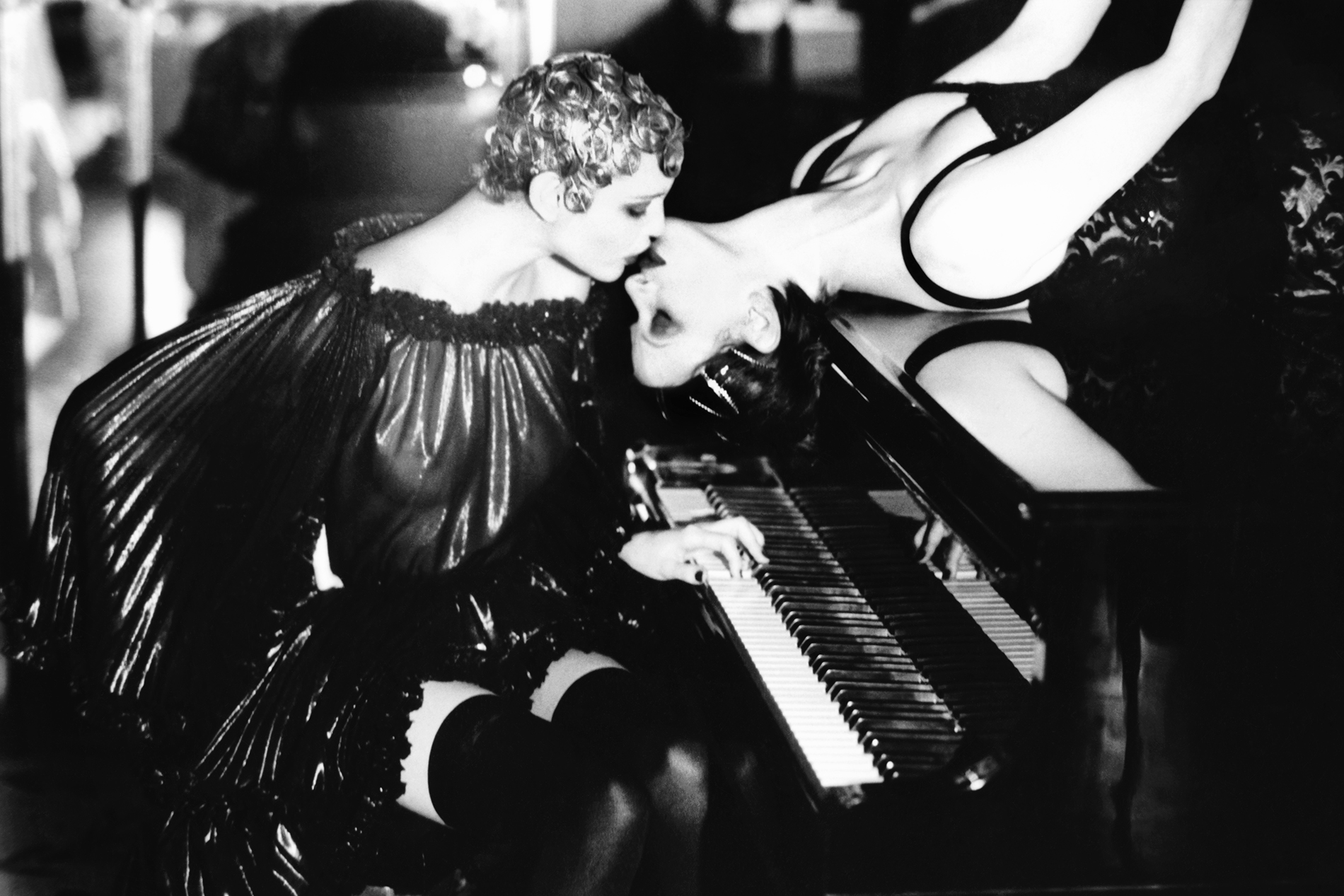 two women kissing on a grand piano