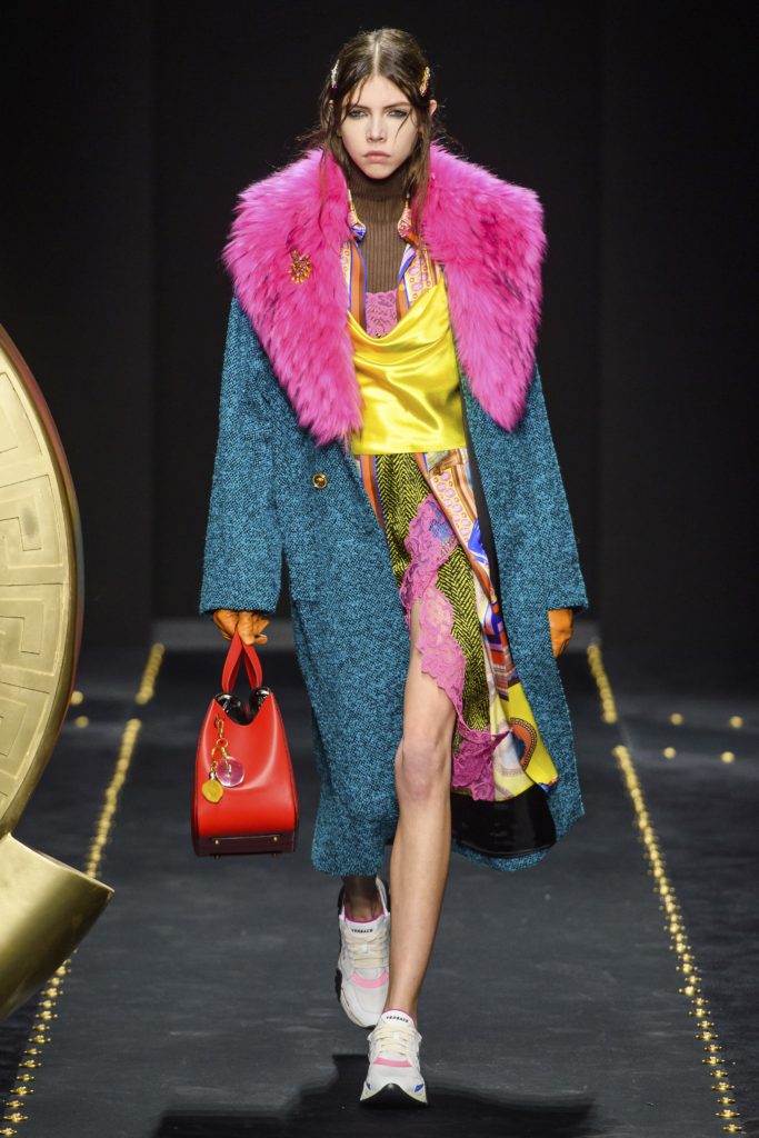 Versace Fall 2019 Runway Show-Model wearing black leather and lace tunic with gold staps, blue sweater and red shoes with blue socks