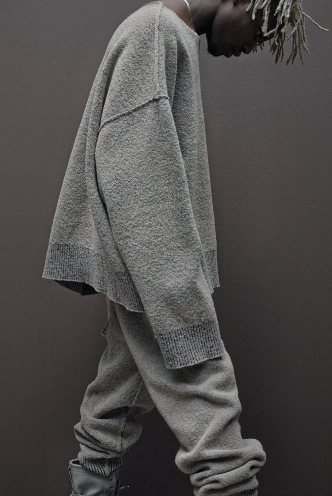 Kayne West Yeezy Model with short platinum dreads an oversized grey sweater , grey leggings and boots