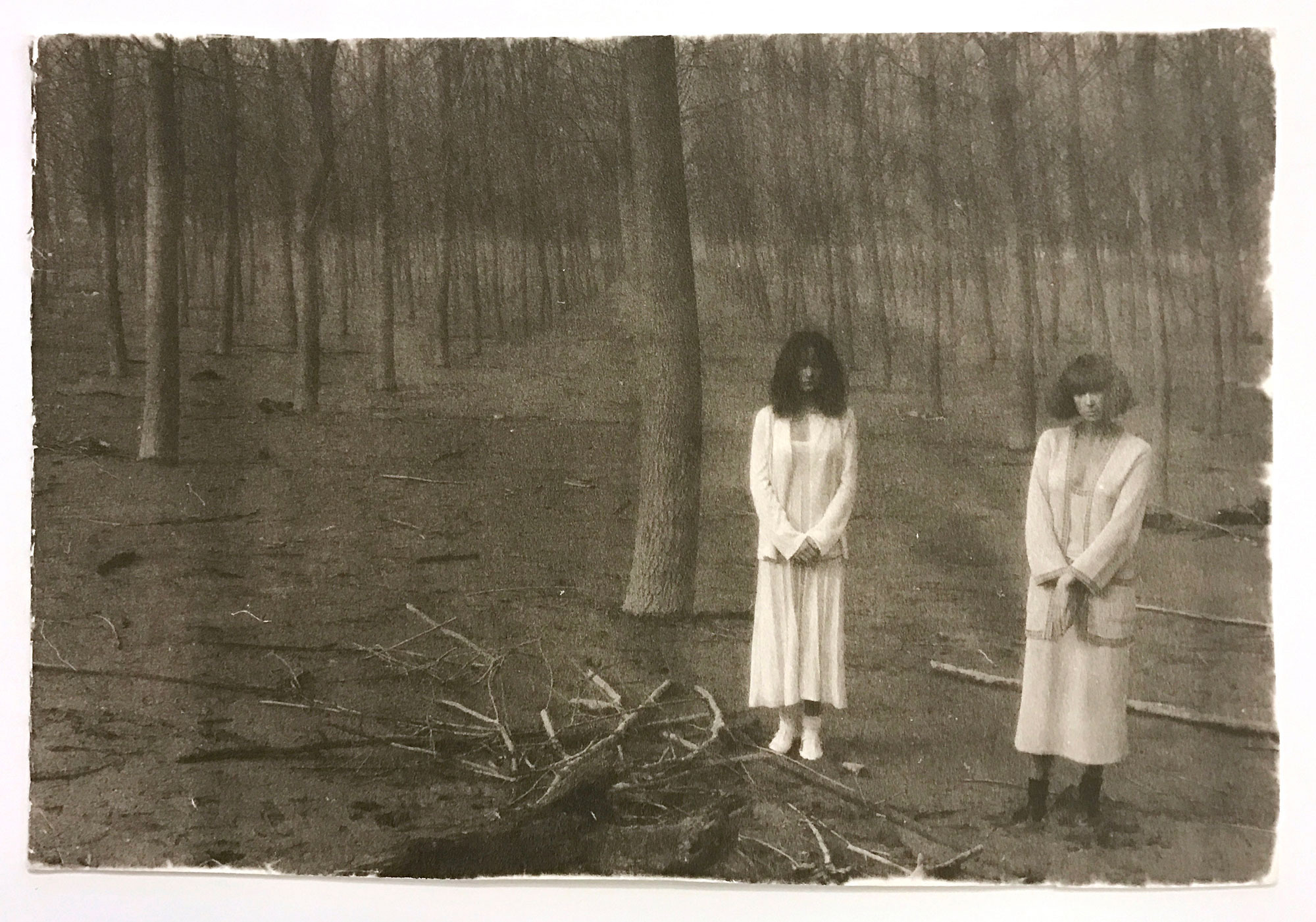 two women wearing white stand side by side in a dead forest