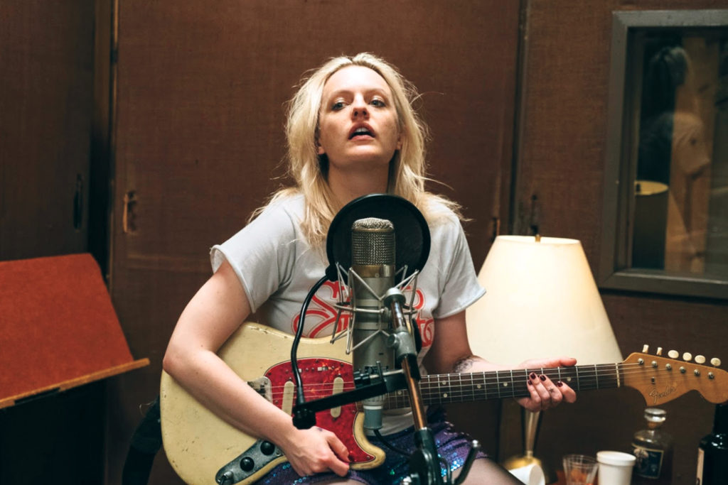 elisabeth-moss-in rock and roll film her-smell in music studio behind a mic holding a Fender electric guitar