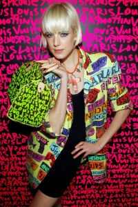 Stephen Sprouse Louis Vuitton Collaboration Image of Model holding a Louis Vuitton Sprouse Grafitti bag against a Sprouse Grafitti wall in hot pink type