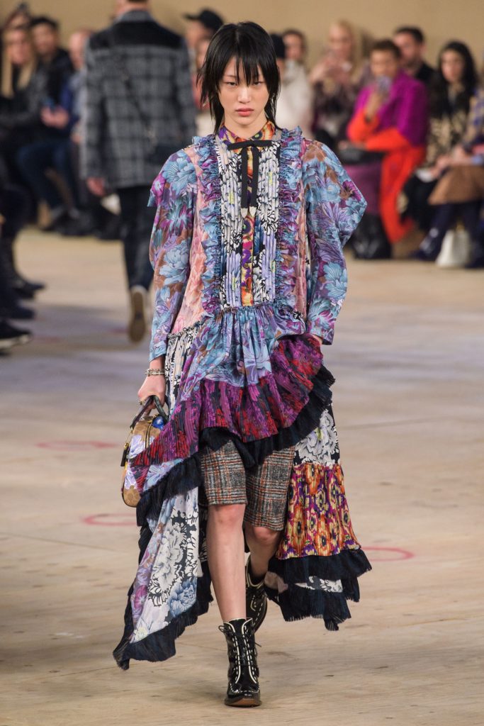 COACH Runway Fall 2019 Model Wearing Gypsy inspired floral dress with skinny black bow tie_plaid shorts and pointed toe black tie boots with white trim