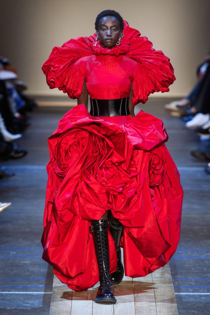 MCQUEEN Fall 2019 Runway Model Wearing Amazing Scupltural Red Dress with Black Leather Belt and Black Lace Up Military Inspired Boots