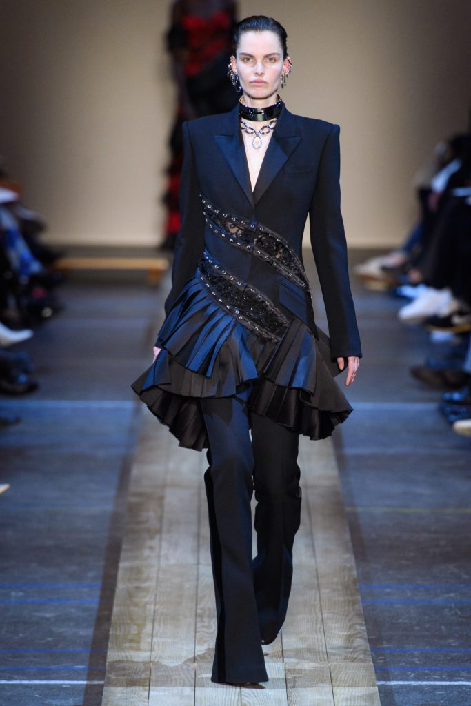 MCQUEEN Fall 2019 Runway Model Wearing Navy and Black Tuxedo Inspired Suit with Studded belts and jewelry
