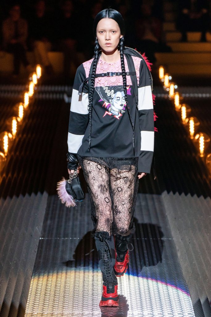 PRADA Runway Fall 2019 Model looking punky wearing black t-shirt with image of madeline kahn as Mrs Frankenstein in Young Frankenstein and black red lace up boots at black patterned stockings