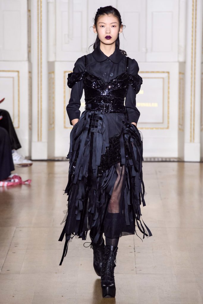SIMONE ROCHA Fall 2019 Runway Model Wearing an amazing black dress with black sequined bustier over black dress with layers of cut black long ribbons and black lace up platform boots