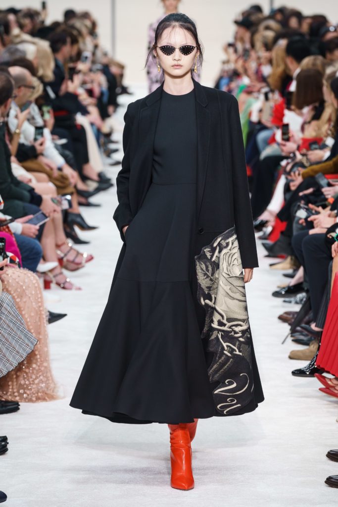 VALENTINO Fall 2019 Runway Model wearing black studded sunglasses black long coat and red pointed toe boots