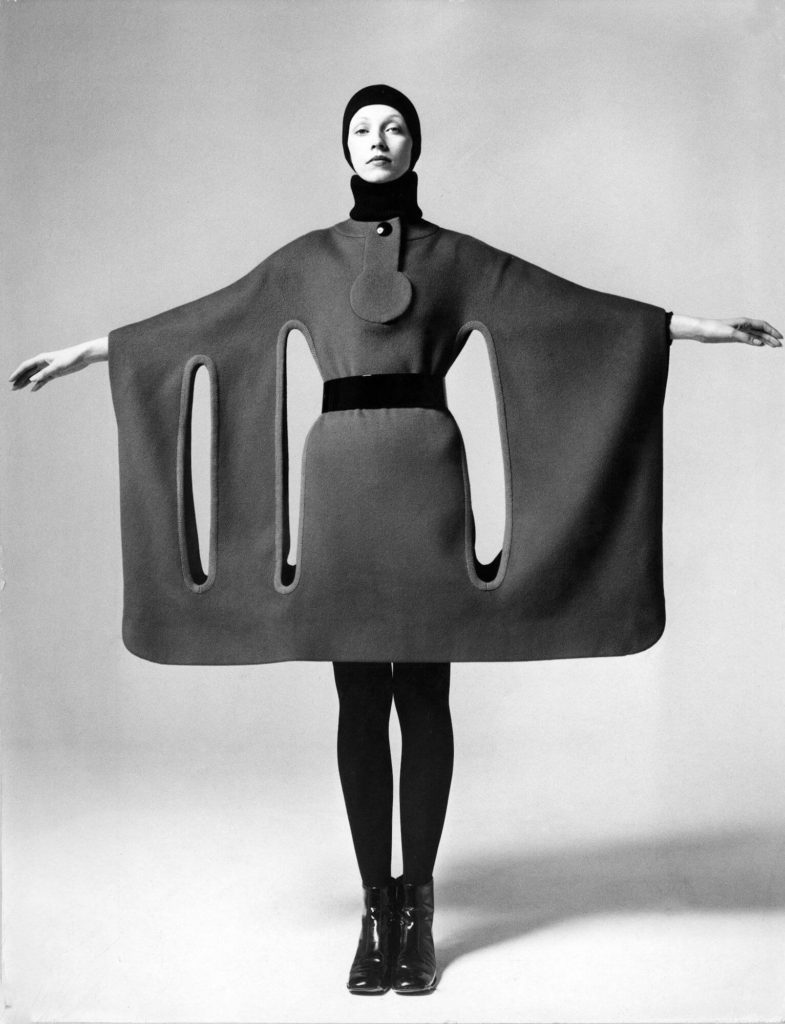 Pierre Cardin Model Holding Her Arms Out to Show a Wide Horizontal Dress form fitting at the body and with long thin vertical circles running below her armpits and Beatle boots