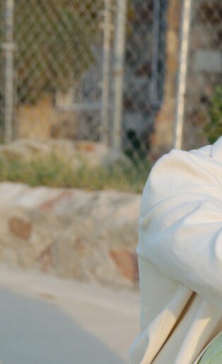 Khalid in white jacket sitting next to chain linked fence