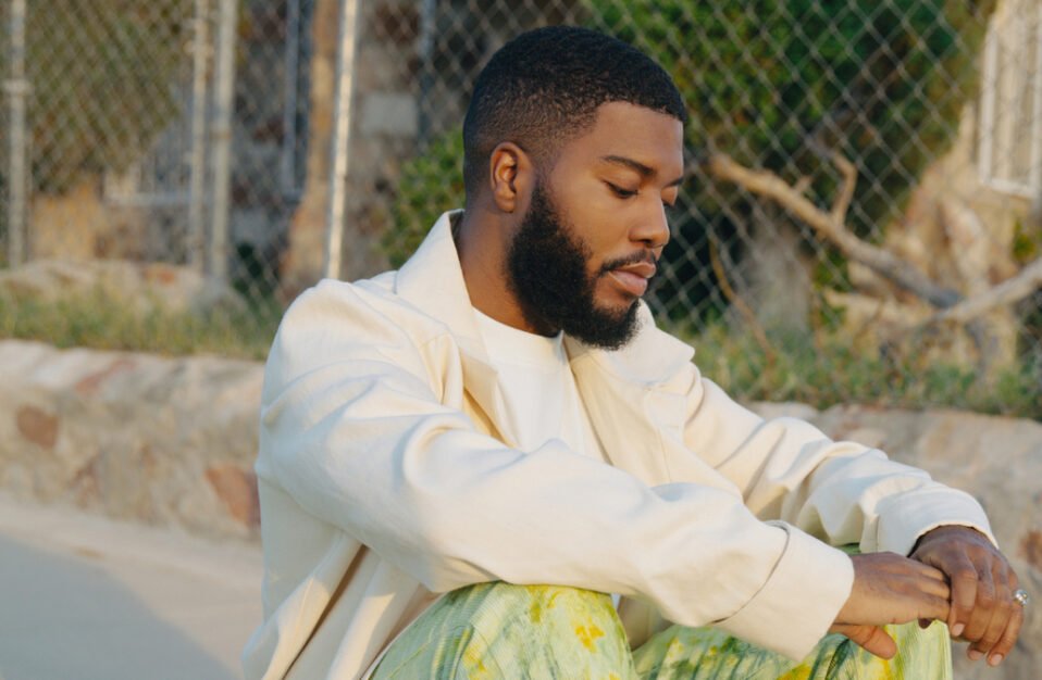 Khalid in white jacket sitting next to chain linked fence