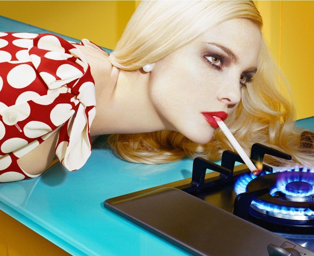 Miles Aldridge Image of Woman Lighting Her Cigarette on a stove burner flame