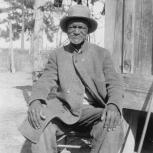 West Brady Ex Slave Sitting In front of his Slave Cabin