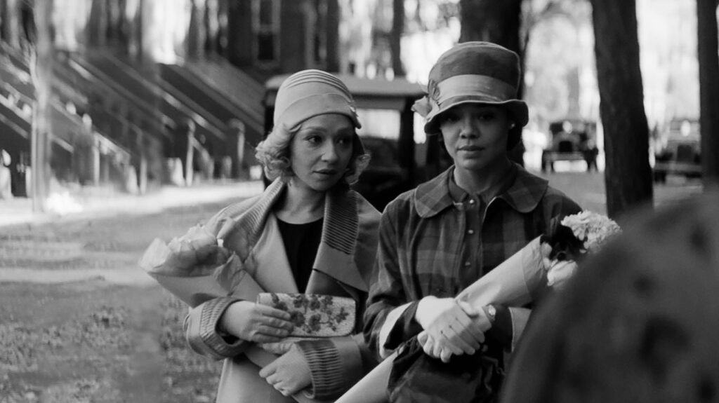 Ruth Negga holding a floral wallet and Tessa Thompson holding a bouquet of flowers in the Passsing